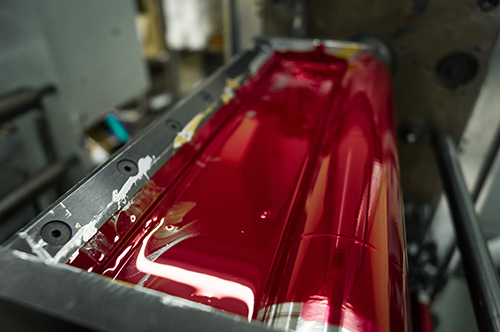 Magenta ink in the paint system compartment of a modern flexographic printing press in a print shop. Red paint in the ink feeder on the printing cylinder. Selective focus.